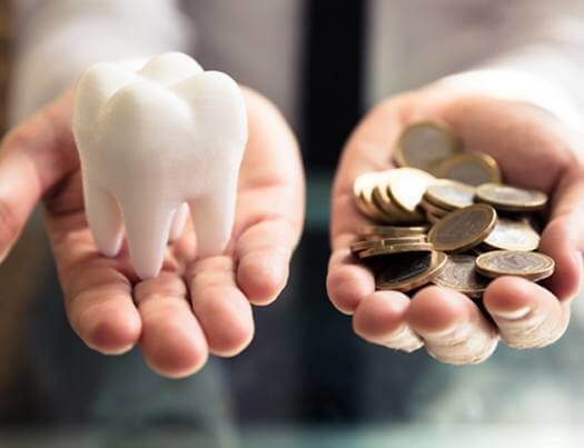 Cost of avoiding the dentist, hand holding tooth and hand holding coins